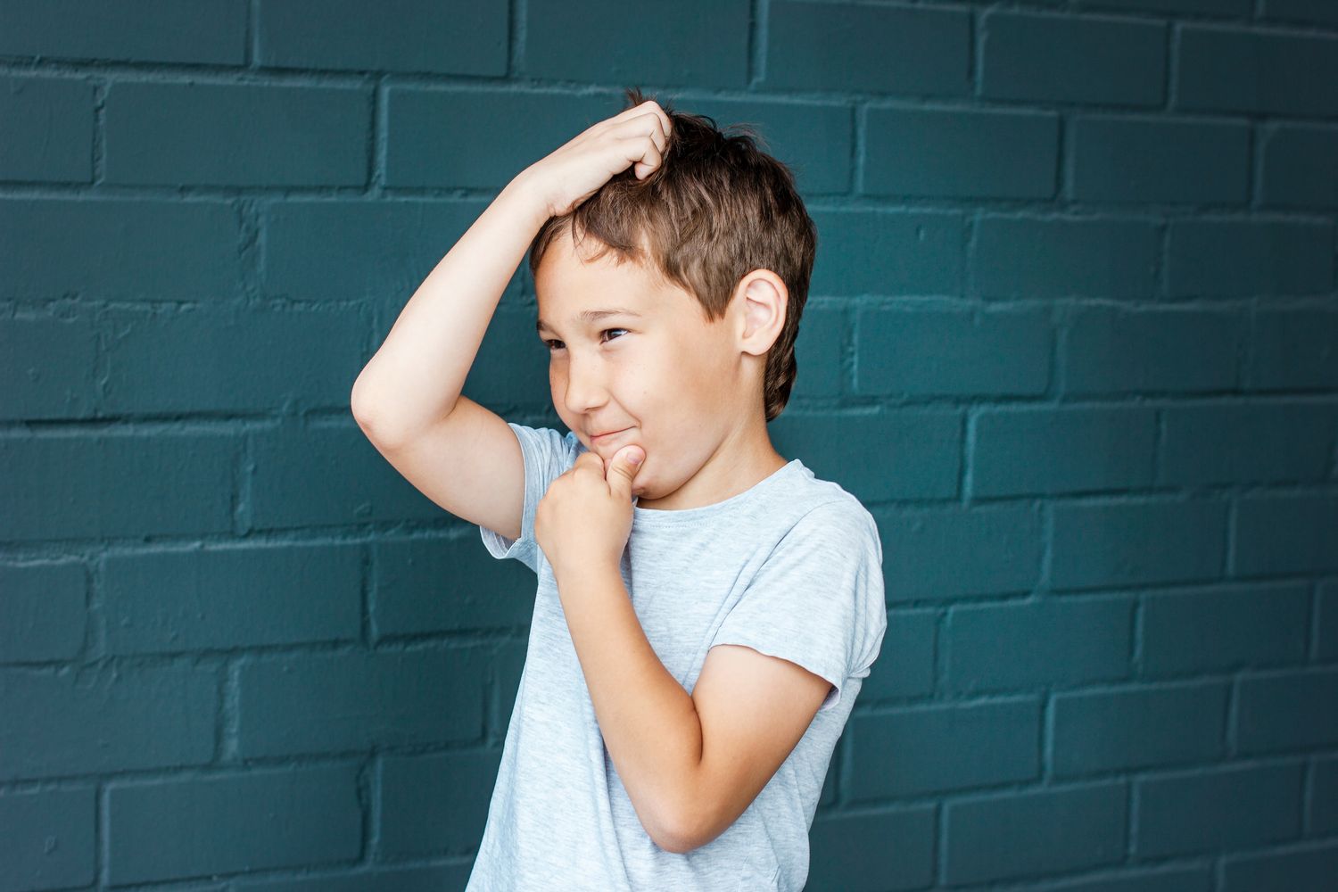 A boy touching his hair against a brick wall